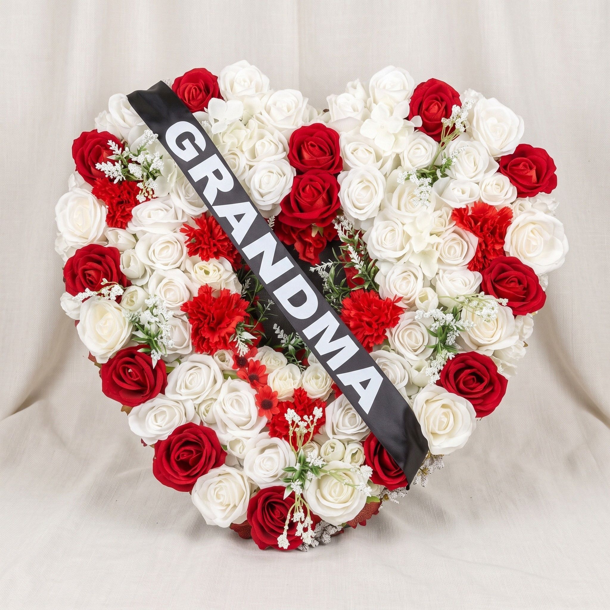 Heart filled with white and red roses, red carnations and sprigs of baby's breath, with a black sash across it reading "GRANDMA" in white letters.