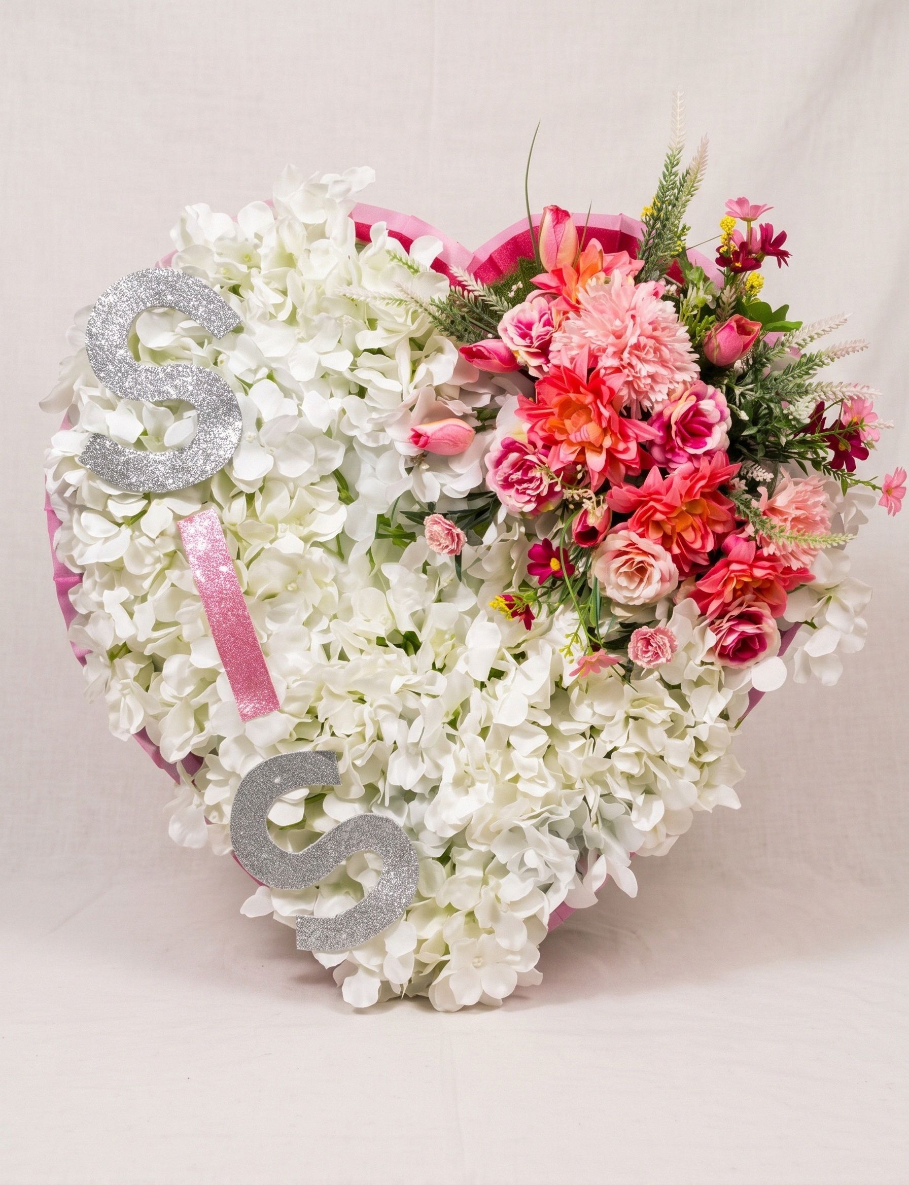Heart of white hydrangeas edged in pink, with a spray of pink roses, coral dahlias and greenery at the top right, and silver glitter letters spelling "SIS" down the left side.